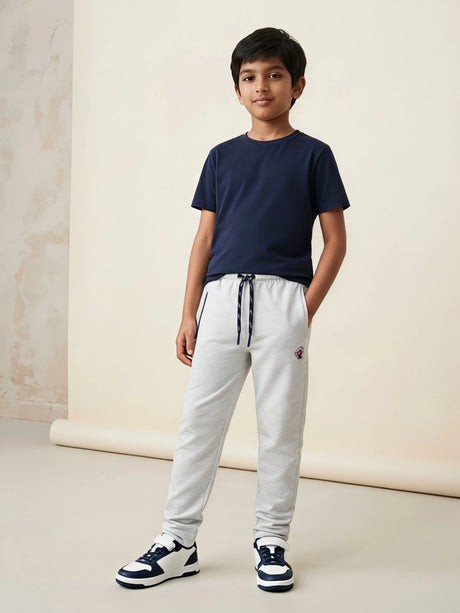 Young boy wearing light grey casual trackpants with an elastic drawstring waist and side pockets paired with a navy blue t-shirt