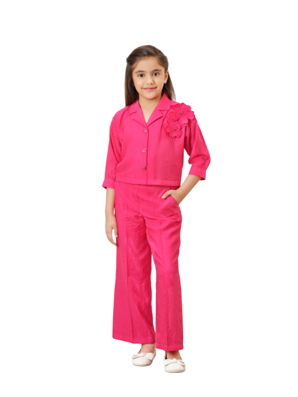 Young girl wearing a bright fuchsia pink two-piece set consisting of a collared, three-quarter sleeve crop shirt with 3D flower detailing on the shoulder, and matching wide-leg palazzo pants.