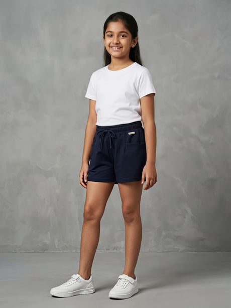 A young girl smiling while wearing a pair of dark navy blue casual shorts with an adjustable drawstring waist and front pockets, paired with a white t-shirt.