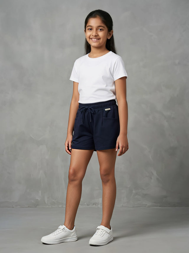 A young girl smiling while wearing a pair of dark navy blue casual shorts with an adjustable drawstring waist and front pockets, paired with a white t-shirt.