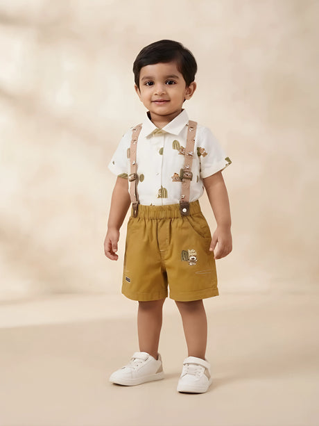 Infant boy wearing a cream short-sleeve printed shirt and brown suspender shorts dungaree set.