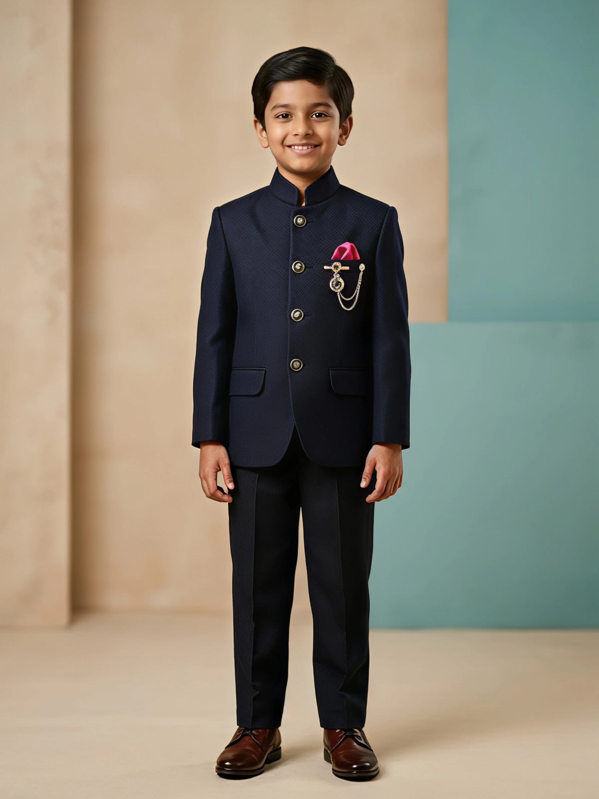 Young boy wearing a navy black tailored Jodhpuri suit set with metallic buttons, pink pocket square accent, and matching formal trousers.