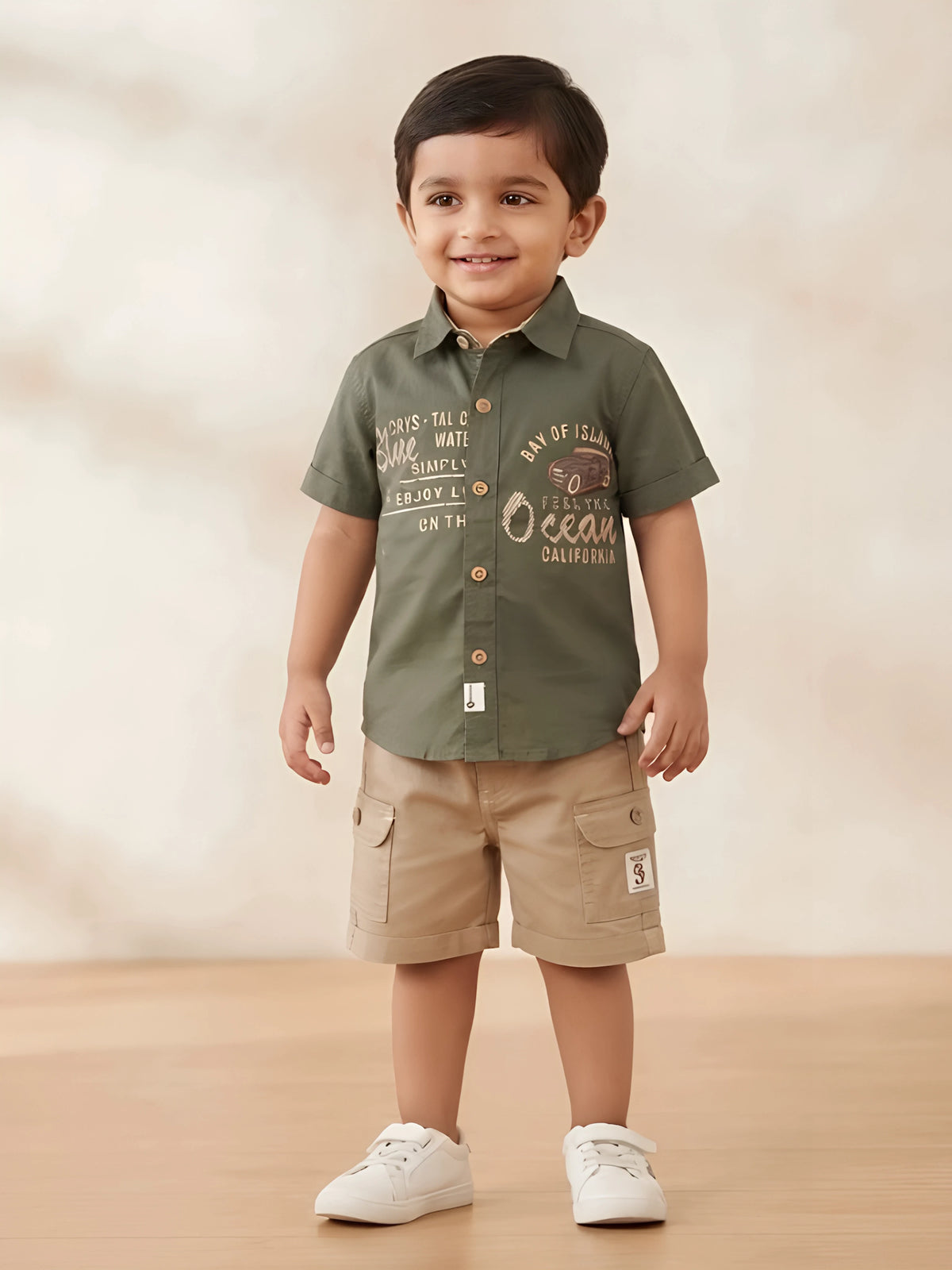 Young boy wearing an olive green short-sleeve printed shirt with a collar and beige cargo shorts with side flap pockets.
