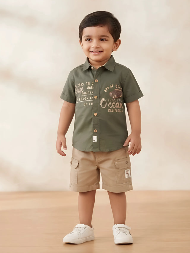 Young boy wearing an olive green short-sleeve printed shirt with a collar and beige cargo shorts with side flap pockets.