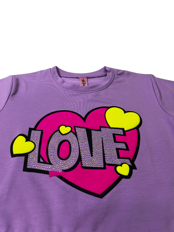 Girls' short-sleeve lavender/purple top with a large central graphic featuring a pink heart, the word 'LOVE' in white sequins, and small yellow hearts.

Export to Sheets