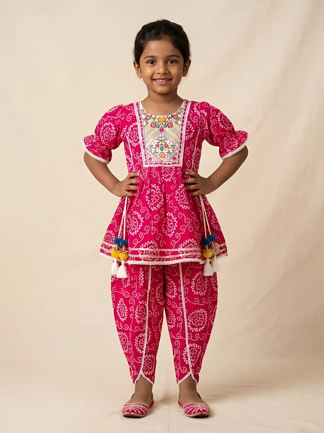 Young girl wearing a vibrant pink bandhani print kurti and matching dhoti pants set with embroidered neck yoke