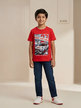 Young boy wearing a bright red crew neck t-shirt with a race car graphic print paired with dark jeans.