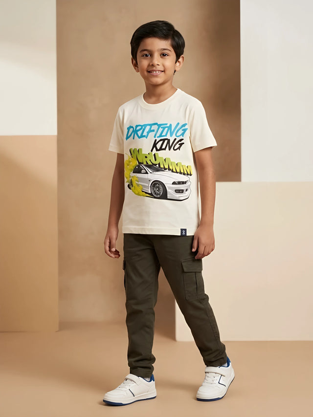 Young boy wearing a cream short-sleeve t-shirt with a blue and yellow "Drifting King" race car graphic print paired with olive cargo pants