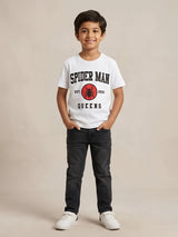 Young boy wearing a white short-sleeve graphic t-shirt with Spider-Man text and logo on the front paired with dark jeans.