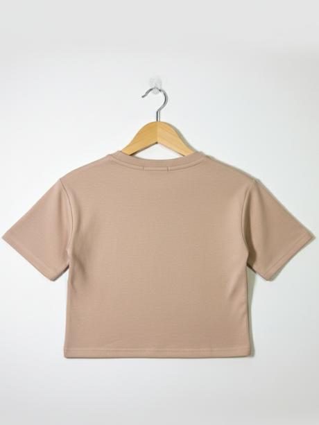 Front view of a girls' nude/tan short-sleeve cropped t-shirt with a thin, contrasting bronze floral outline embroidery on the chest, hanging on a wooden hanger.