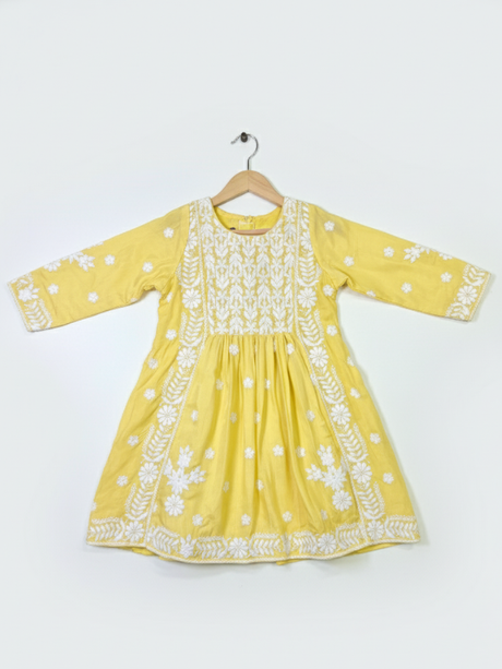 Full-length image of a young girl wearing a bright yellow, white-embroidered, flared frock (kurta) with matching yellow pants and a white dupatta.