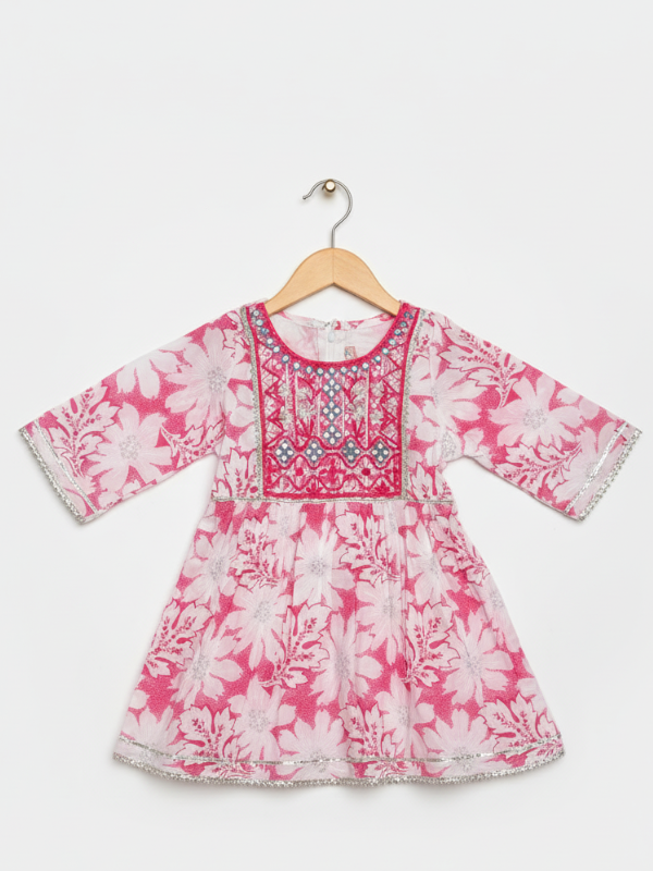 Front view of a girls' 3/4 sleeve pink and white floral-printed peplum top (kurti) with a heavily embroidered and mirror-work detailed yoke, hanging on a wooden hanger.