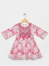 Front view of a girls' 3/4 sleeve pink and white floral-printed peplum top (kurti) with a heavily embroidered and mirror-work detailed yoke, hanging on a wooden hanger.