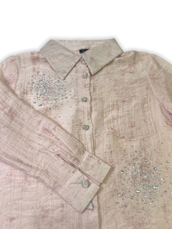 Front view of a girls' sheer peach long-sleeve button-up shirt with silver rhinestone clusters on the chest, hanging on a wooden hanger.