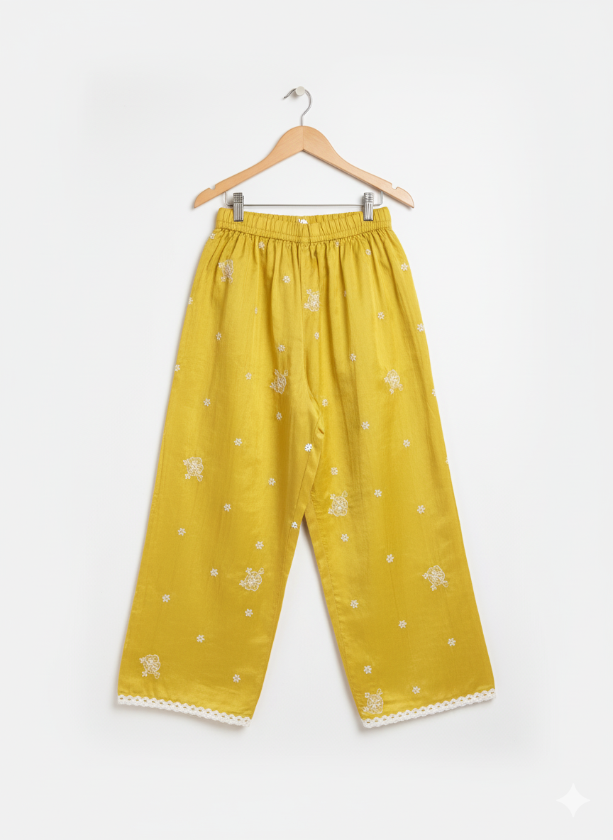 Front view of girls' wide-leg yellow palazzo pants with scattered white floral embroidery and a white lace trim on the hem, hanging on a wooden hanger.