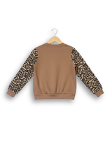 Front view of a girls' brown sweatshirt with long leopard print sleeves and a framed graphic of a girl on the chest, hanging on a wooden hanger.