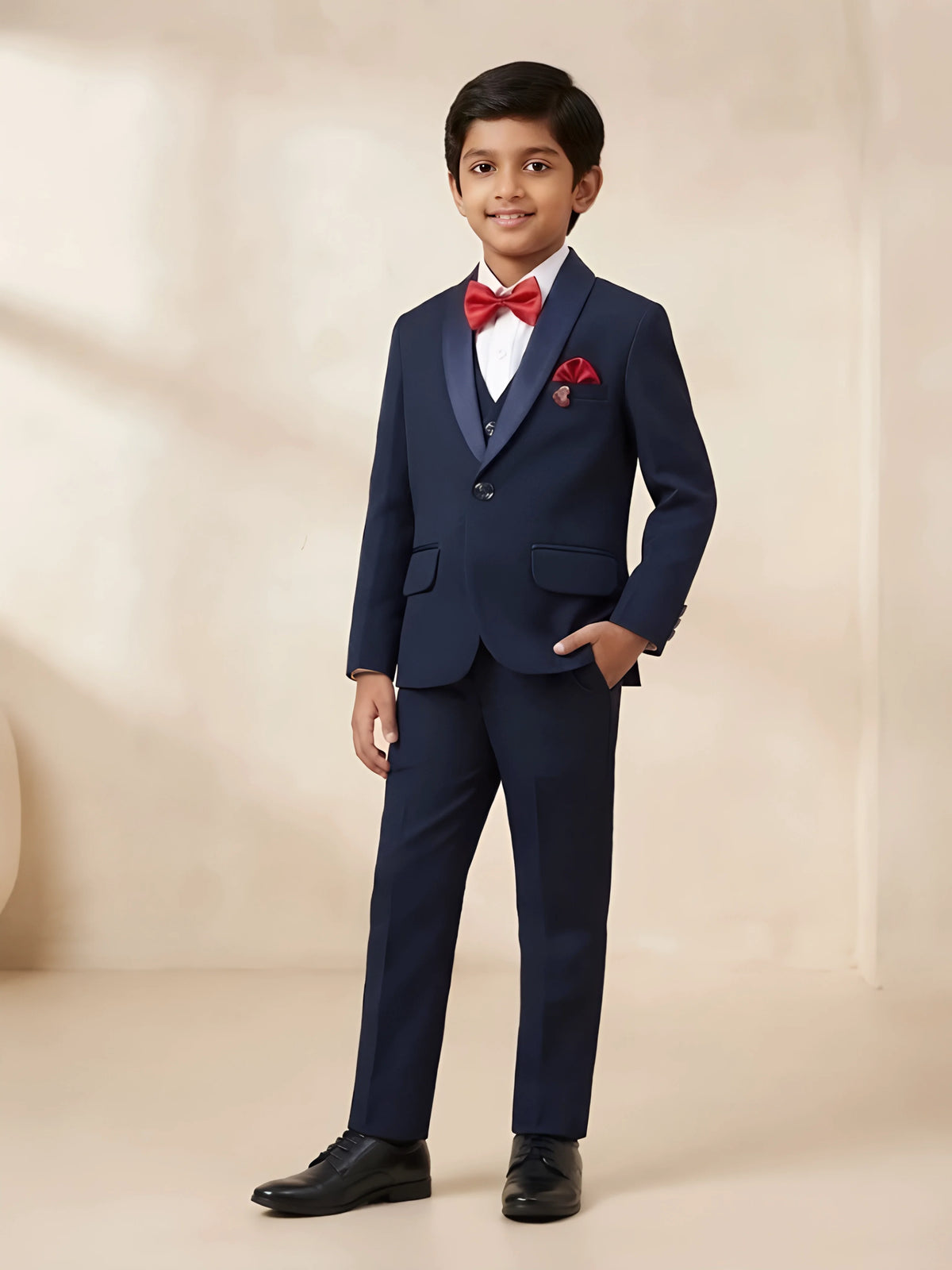Boys navy blue tuxedo coat suit set with satin shawl lapel blazer, white shirt, waistcoat, trousers, red bow tie, and red pocket square