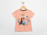 Disney Frozen Anna and Elsa hugging graphic print inside a colorful floral wreath on a peach/coral girls' short-sleeve T-shirt hanging on a wooden hanger against a white background.
