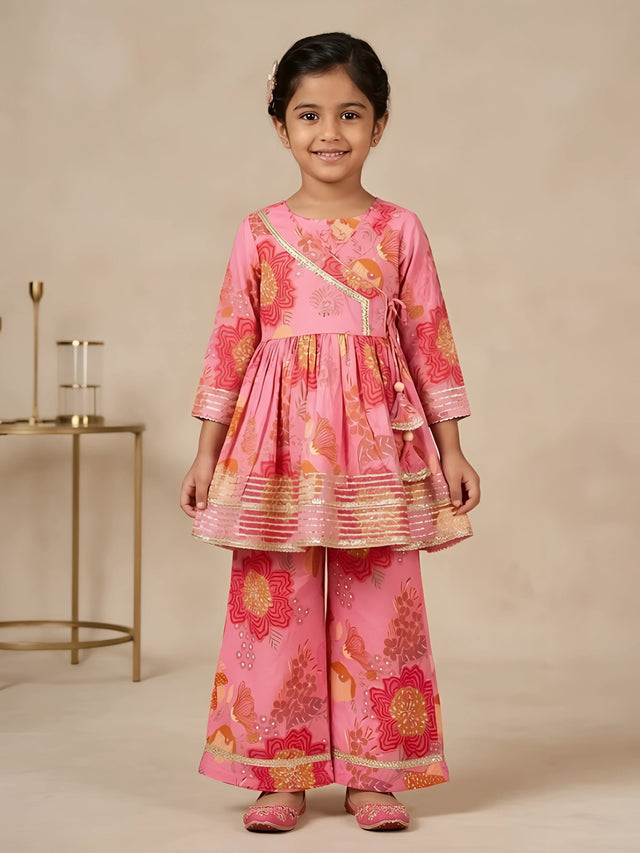 Young girl wearing a pink floral printed Angrakha style peplum kurti with flared sharara bottoms and gold lace trimming
