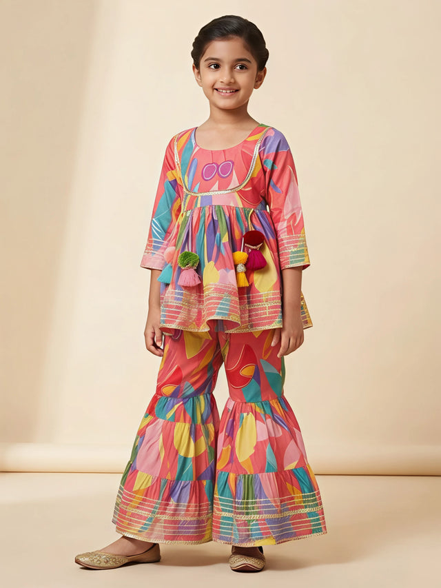 Young girl wearing a peach multi-color printed ethnic sharara set with tassel details and lace borders.