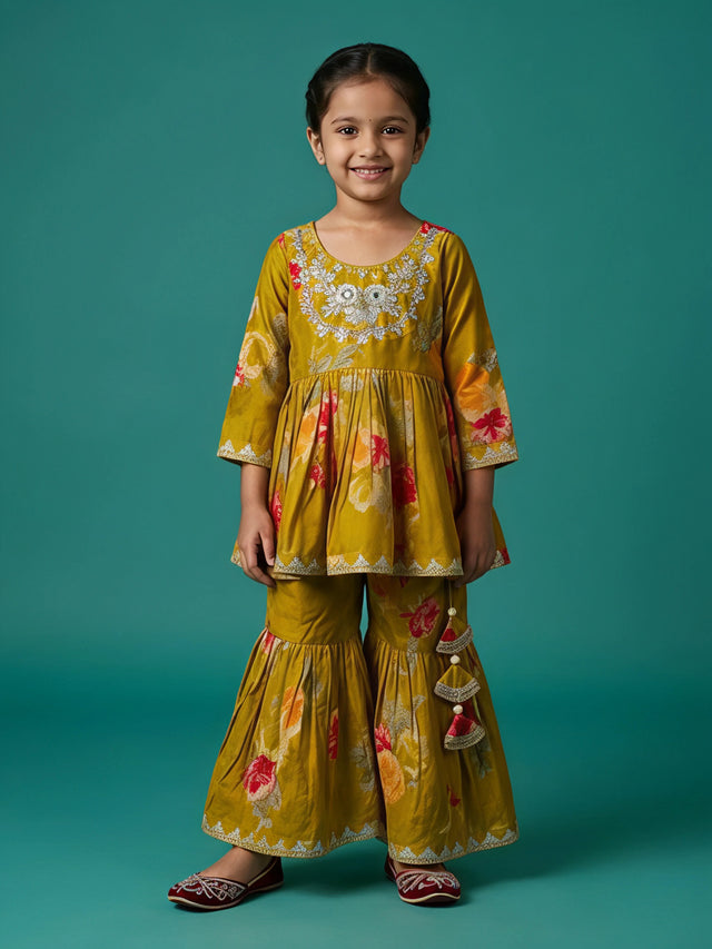 Young girl wearing an olive green floral printed sharara suit with embroidered neckline and decorative tassels