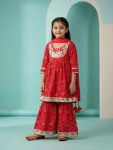 Young girl wearing a vibrant red Bandhani print sharara set with embroidery and matching dupatta
