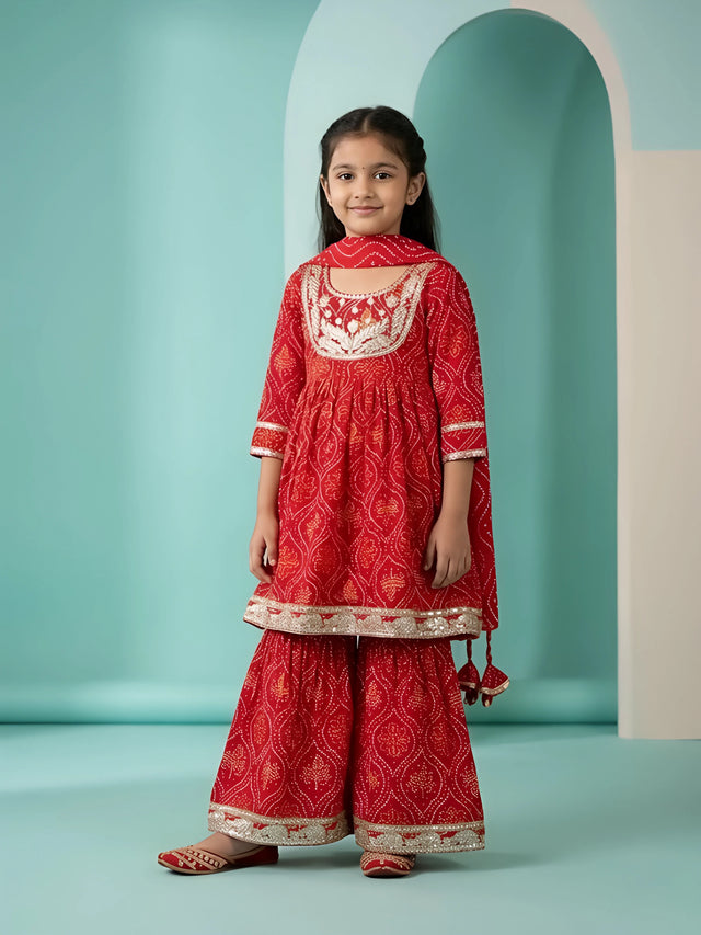 Young girl wearing a vibrant red Bandhani print sharara set with embroidery and matching dupatta