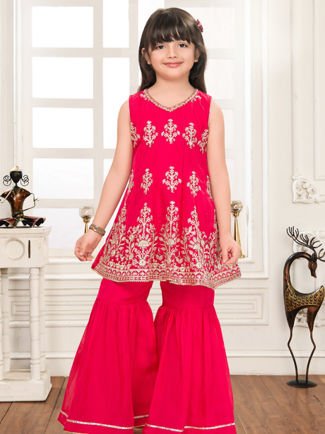 Young girl wearing a vibrant rani pink ethnic set featuring a sleeveless V-neck peplum top with intricate gold embroidery, paired with voluminous tiered sharara pants trimmed with gold lace.