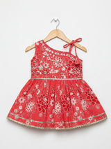 Full-length image of a young girl wearing a coral red and white printed peplum kurta with shoulder ties, wide-leg palazzo pants, and a white-to-red ombre dupatta with silver trim.