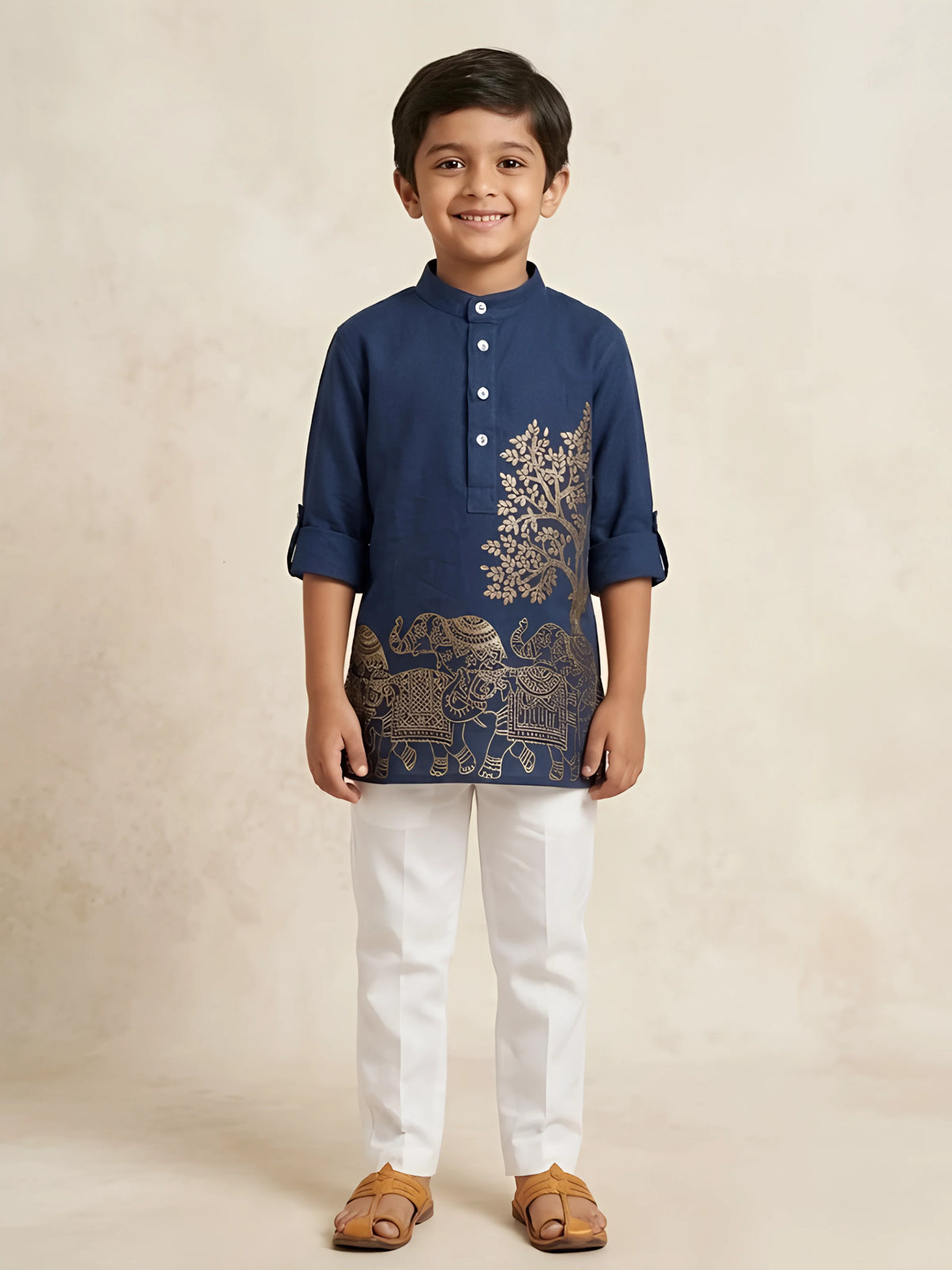 Young boy wearing a navy blue casual shirt with metallic gold tree and elephant prints, mandarin collar, and folded sleeves paired with white trousers.