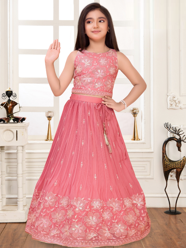 Young girl modeling a sleeveless onion pink lehenga set consisting of an embroidered crop top and a pleated skirt with a large floral embroidered border.