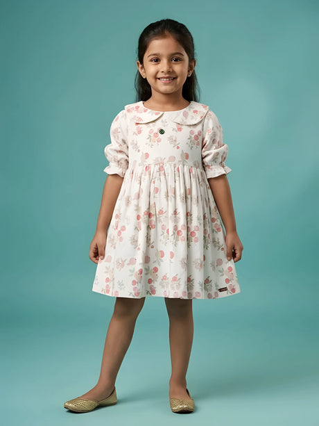 Little girl wearing a cream floral printed frock with a Peter Pan collar and elasticated puff sleeves against a light blue background
