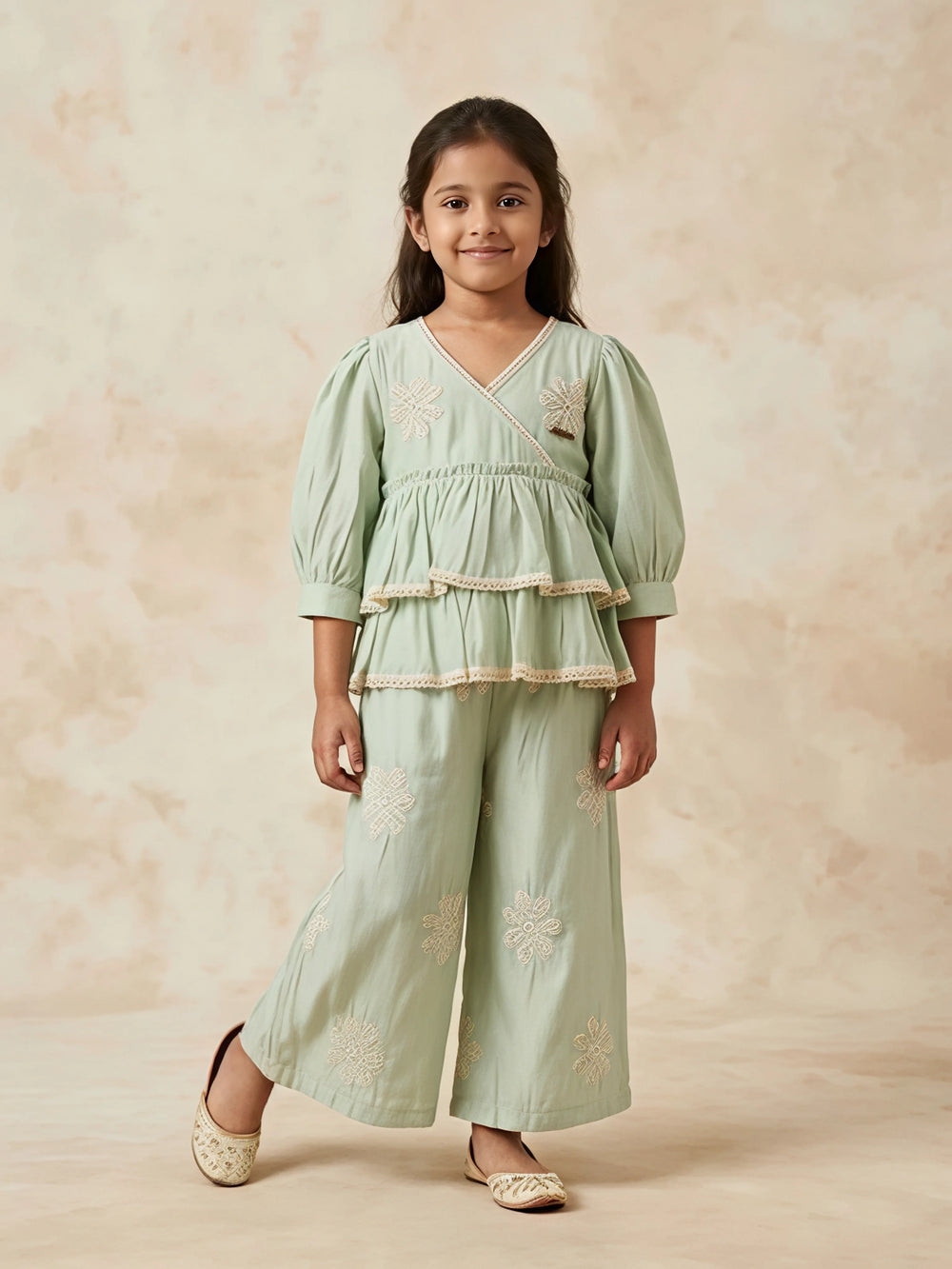 Young girl wearing a light green Angrakha-style tiered kurta with lace trim and matching wide-leg embroidered palazzo pants.