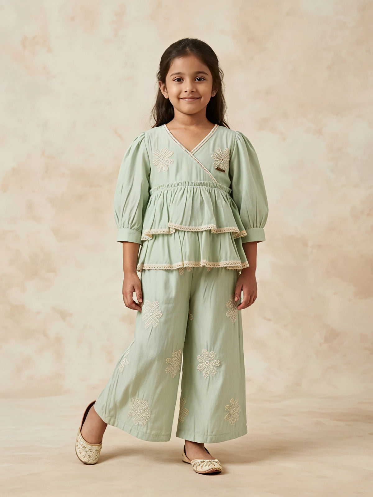 Young girl wearing a light green Angrakha-style tiered kurta with lace trim and matching wide-leg embroidered palazzo pants.