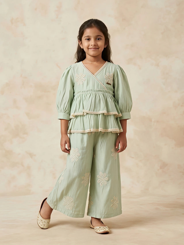 Young girl wearing a light green Angrakha-style tiered kurta with lace trim and matching wide-leg embroidered palazzo pants.