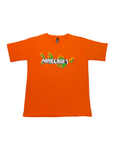 Vibrant Orange boys' short-sleeve T-shirt with the white Minecraft logo and a scattered pattern of green and yellow pixelated blocks graphic printed centrally.