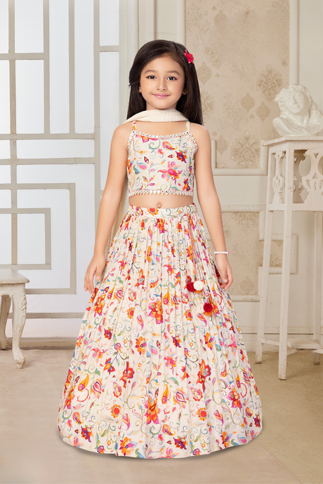 Young girl wearing a sleeveless cream lehenga choli set with an all-over floral print in pink, orange, and yellow, and small mirror details on the crop top.