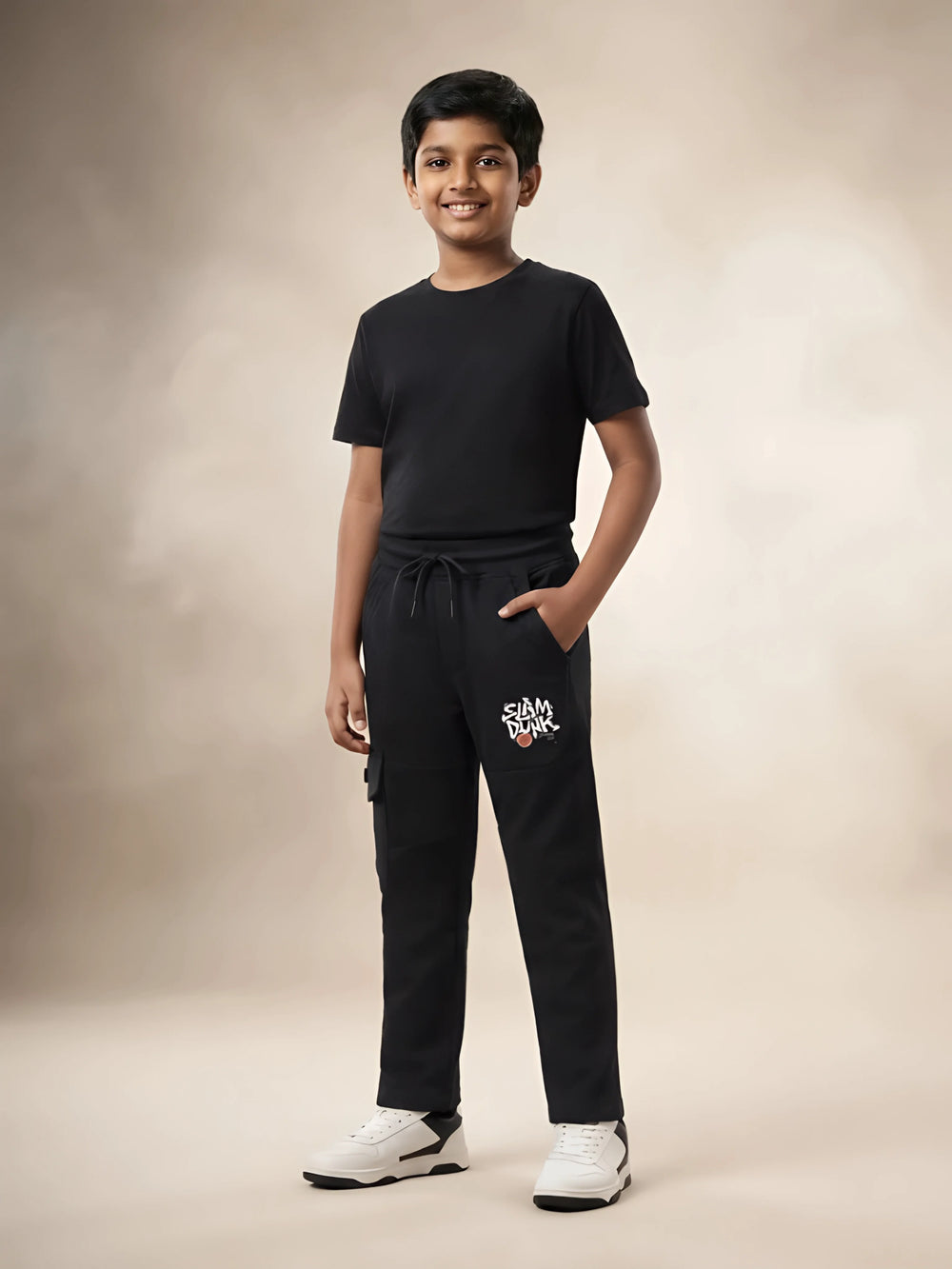Young boy wearing black printed cargo trackpants with side pockets and a black t-shirt