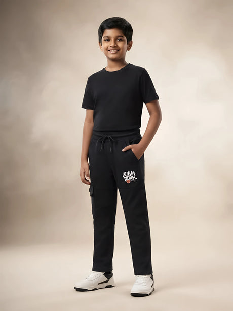 Young boy wearing black printed cargo trackpants with side pockets and a black t-shirt