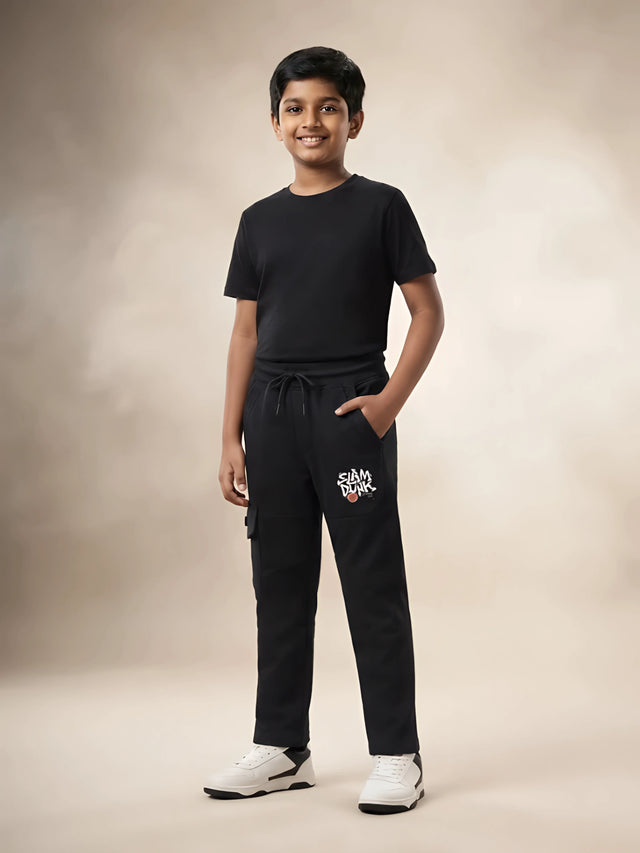 Young boy wearing black printed cargo trackpants with side pockets and a black t-shirt