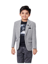 Young boy smiling in a textured light grey blazer with a lapel pin and black pocket square, layered over a black graphic t-shirt and dark grey acid-wash jeans.