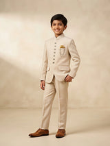 Boy wearing a cream Jodhpuri suit with a mandarin collar, decorative buttons, pocket square detail, and matching trousers