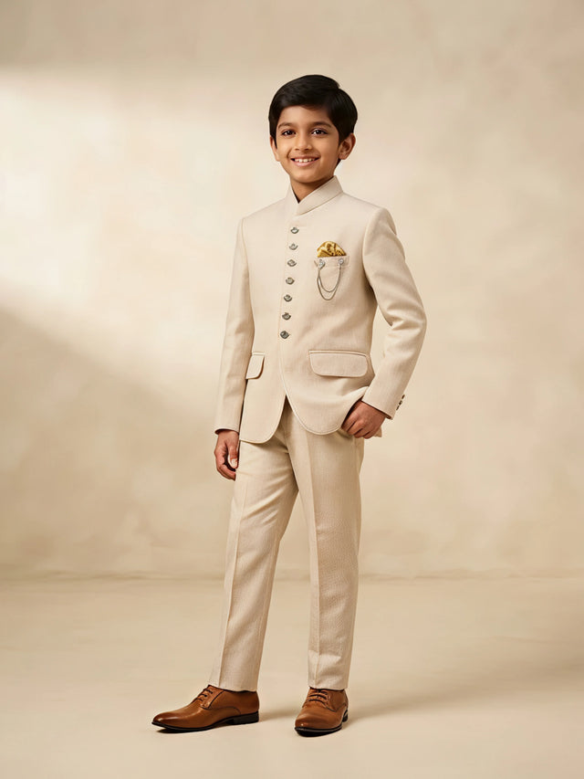 Boy wearing a cream Jodhpuri suit with a mandarin collar, decorative buttons, pocket square detail, and matching trousers