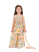 Young girl smiling in a sleeveless cream peasant top with a smocked, multi-color embroidered yoke, paired with matching wide-leg garara trousers featuring a vibrant floral print, holding a matching scarf.
