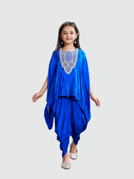 Young girl posing in a vibrant royal blue ethnic set with a flowy, embellished kaftan top featuring silver beading and voluminous matching dhoti trousers, paired with metallic shoes.