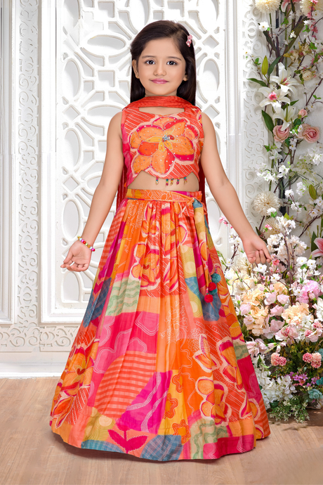 Young girl wearing a sleeveless orange and multi-colored patchwork print lehenga choli set, with a halter-neck crop top and matching scarf.