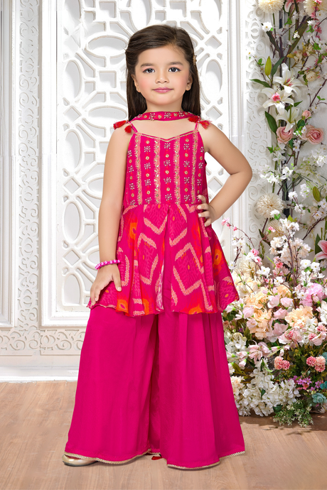 Young girl wearing a sleeveless Rani Pink sharara suit with a peplum top embroidered in gold thread and mirror work, paired with flowing matching sharara pants.