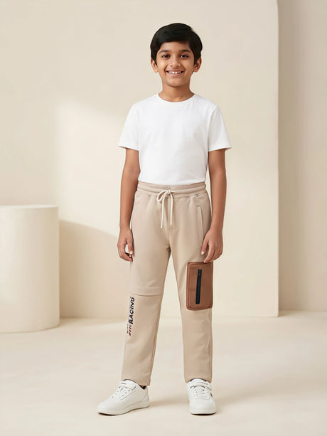 Young boy wearing cream stylish cargo track pants with drawstring waistband and contrast pocket detail