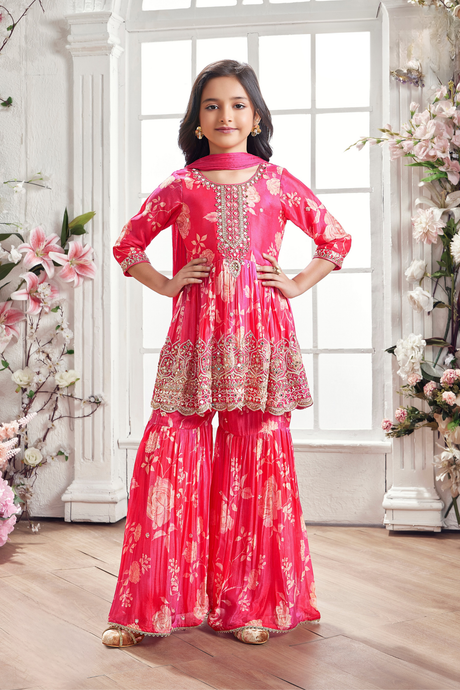 Young girl wearing a full Rani Pink (fuchsia) gharara suit with a floral printed fabric and heavy gold and silver embroidery on the bodice and hem.