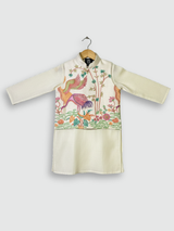 A young boy standing and smiling, wearing a cream/off-white long-sleeved kurta and pajama set with beautiful, detailed multi-color bird and floral embroidery across the chest.